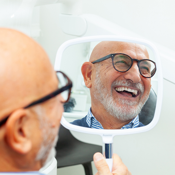 Senior man in the dental chair admiring his new smile in a mirror