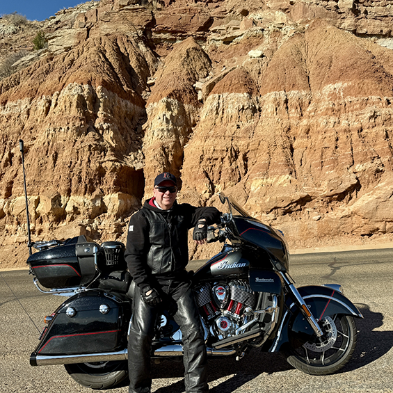 Doctor Hubler standing with his motorcycle on a road by a small cliffside