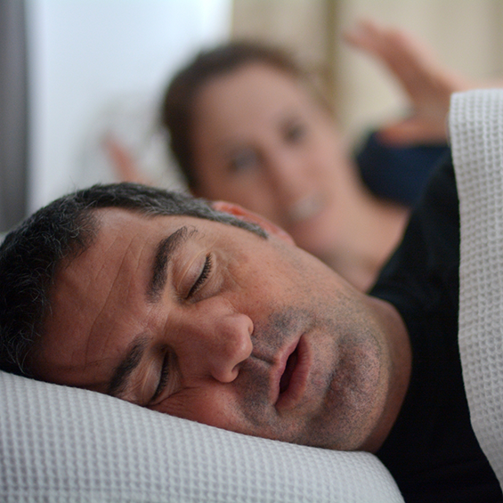 Woman raising her hands in frustration next to a snoring man in bed